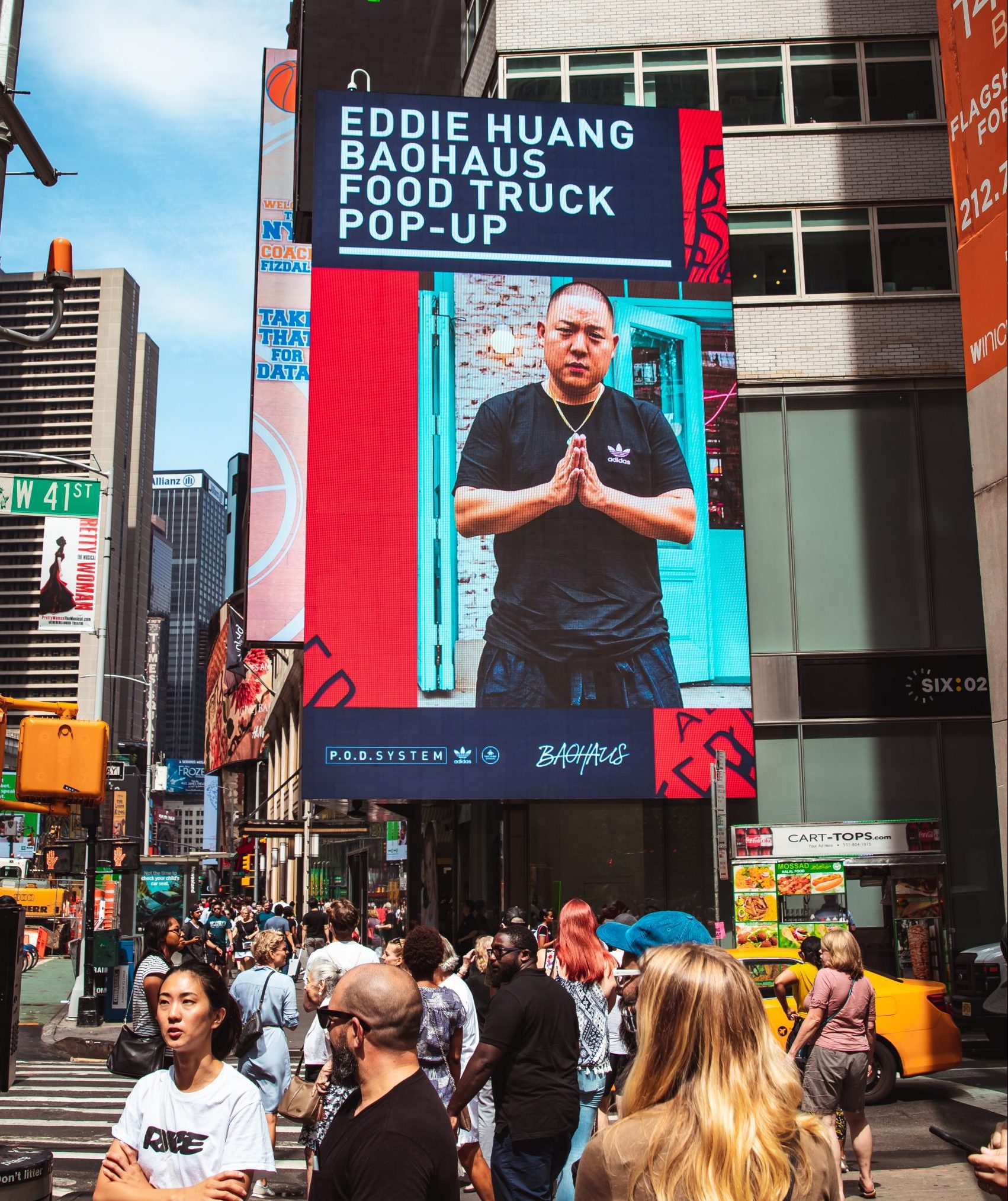 A city square billboard advertises the Eddie Huang Baohaus Food Truck as crowds gather below.
