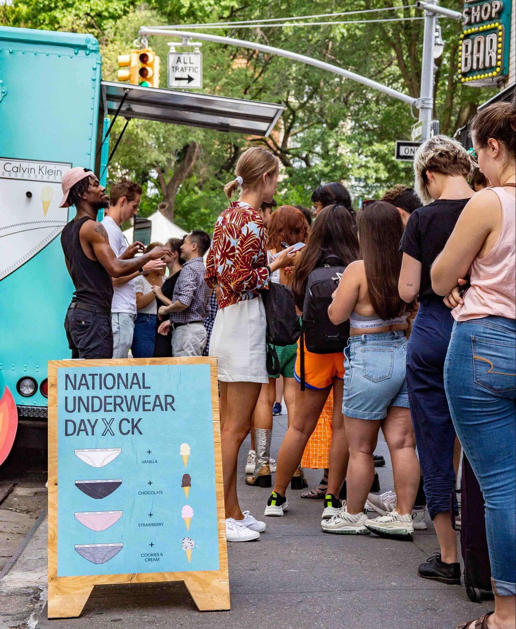People line up on a city sidewalk by a blue truck with a "National Underwear Day" sign.