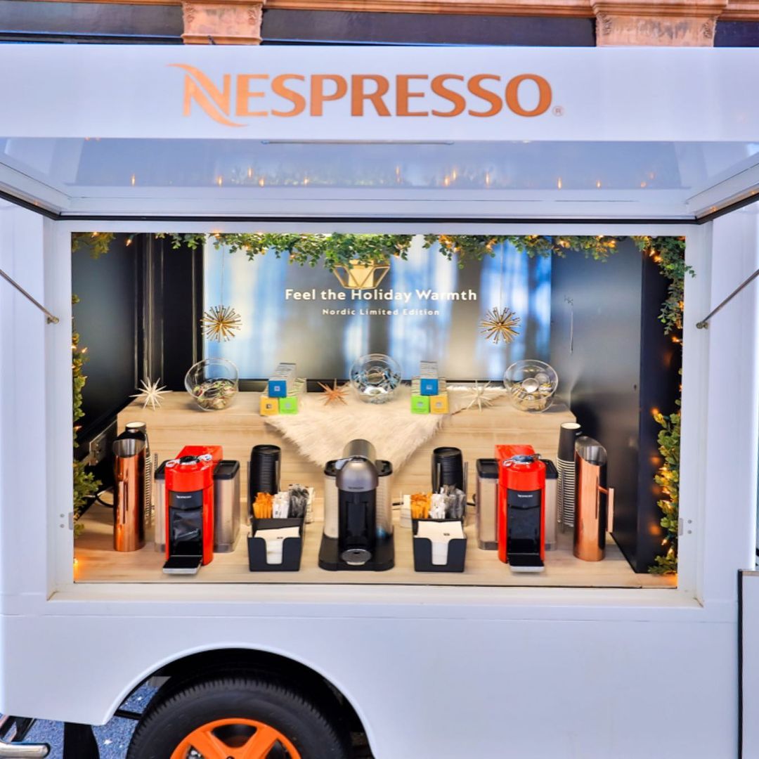 Nespresso machines, capsules, and mugs on a counter with holiday decor and festive message.