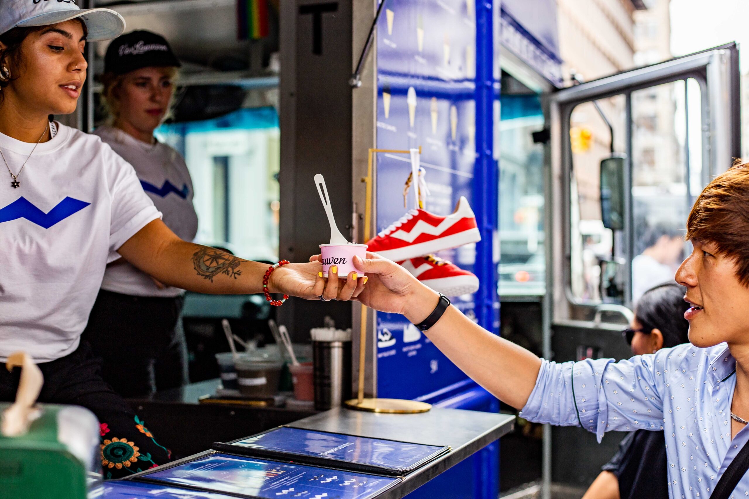 A woman at a food truck gives ice cream to a man; another woman stands inside the truck.