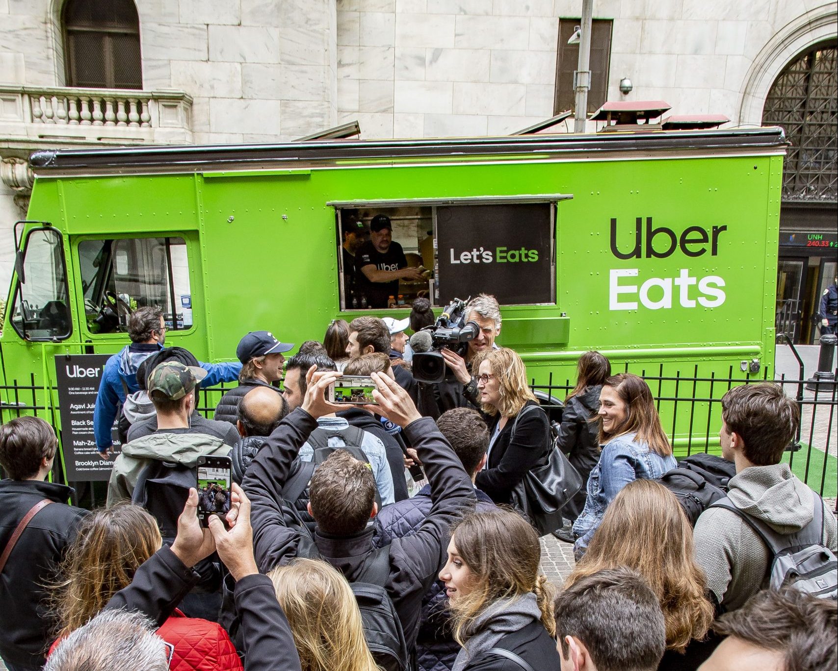 People crowd a green Uber Eats food truck on a city street as someone serves food.