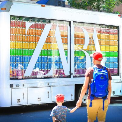 Man and child in red caps stand by a white ZARA truck with shelves of colorful books inside.