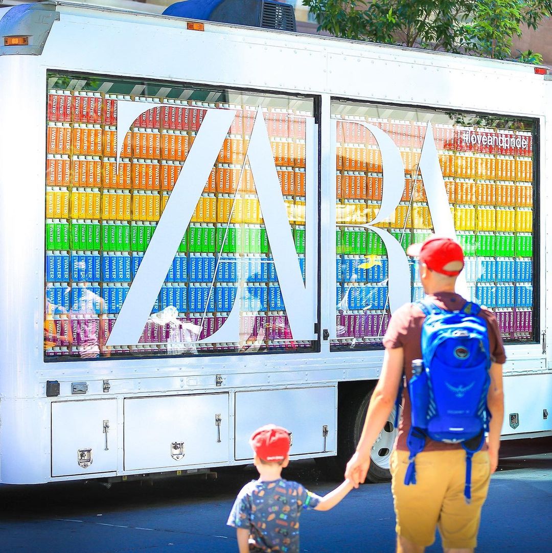 Man and child in red caps stand by a white ZARA truck with shelves of colorful books inside.