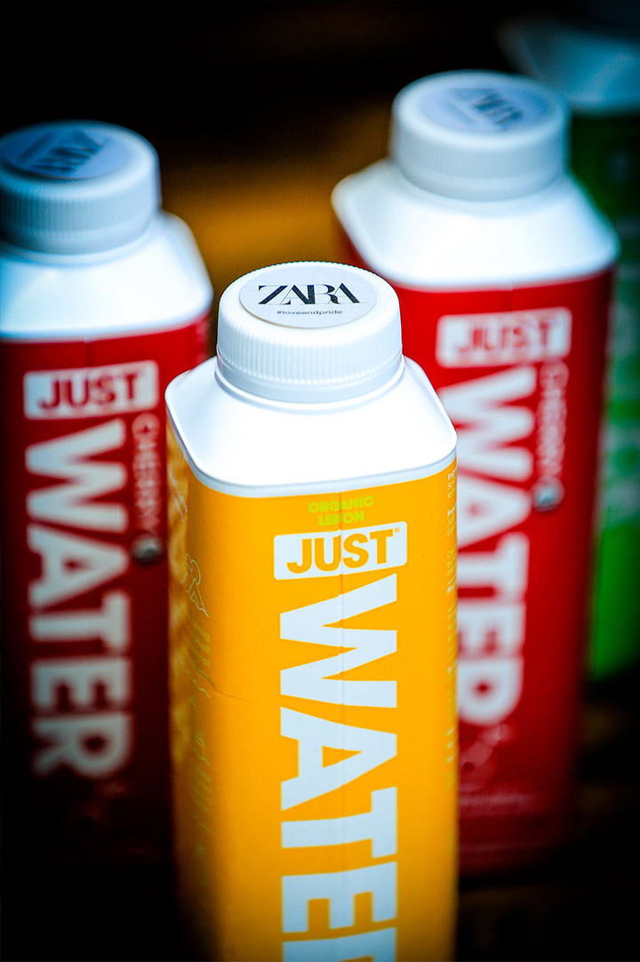 Yellow JUST WATER carton with white cap in front of two red cartons with matching branding.