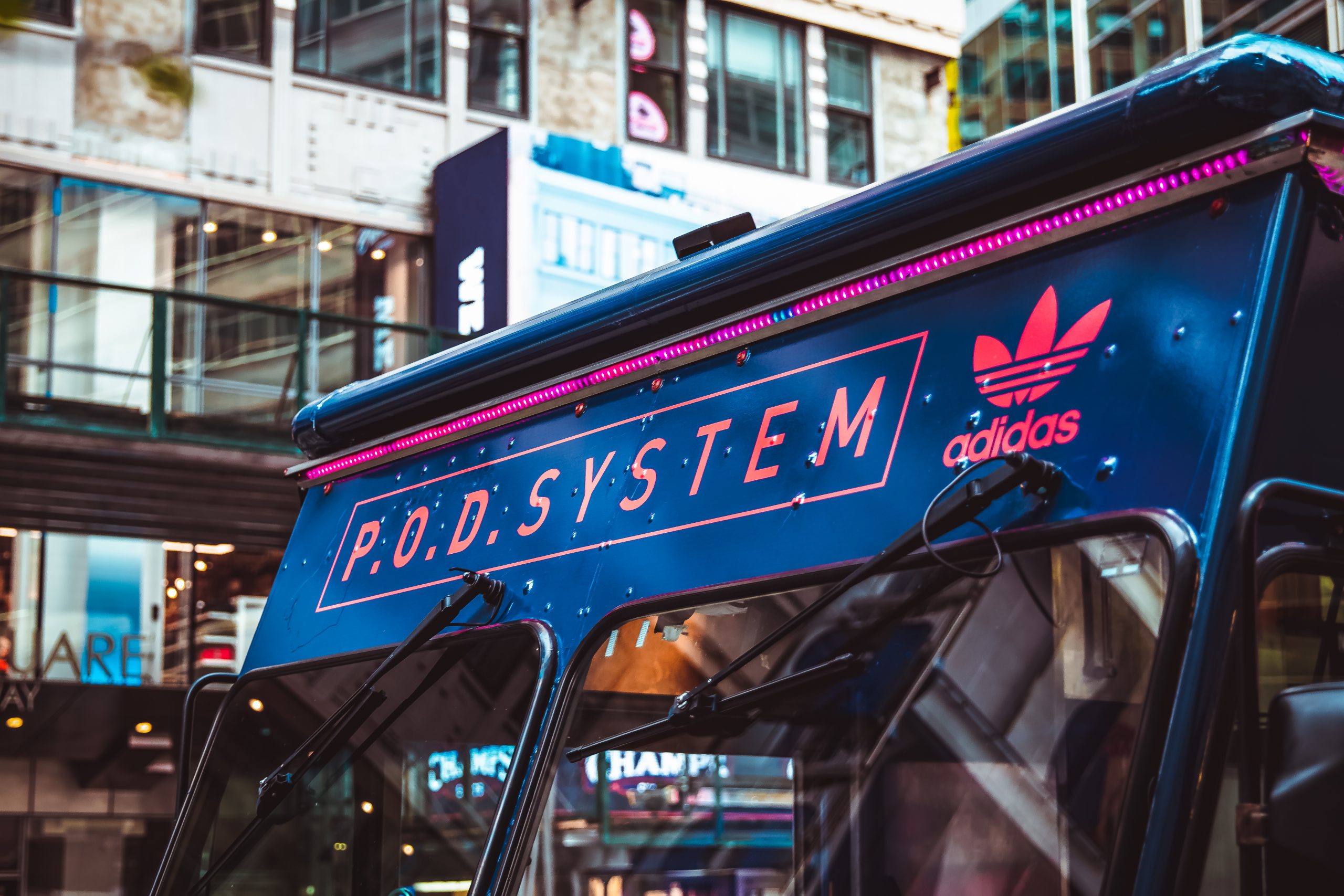 Blue food truck top with pink neon lights, “P.O.D. SYSTEM” and Adidas logo on city street.