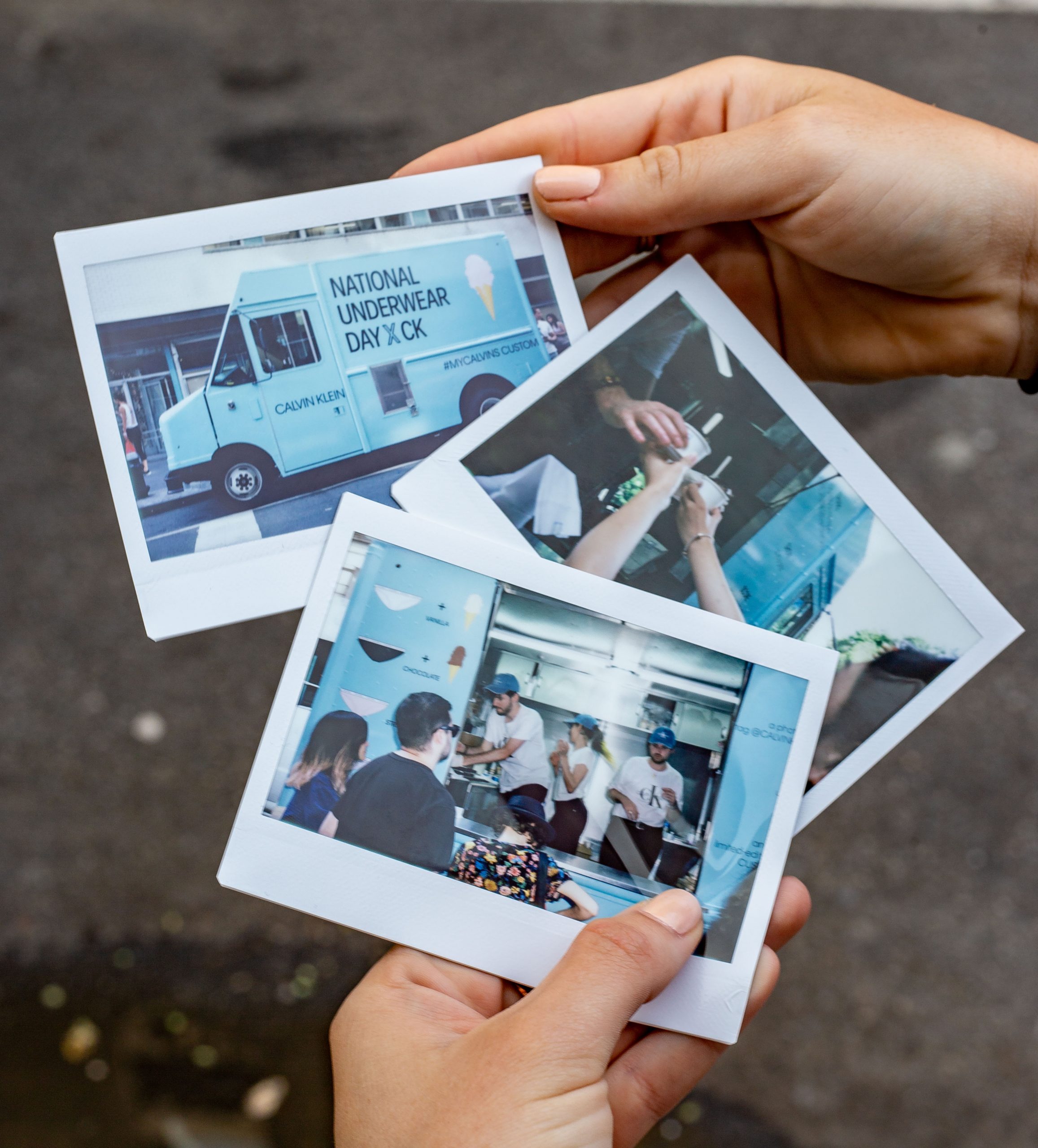 Person holds three instant photos showing people near a blue National Underwear Day truck.