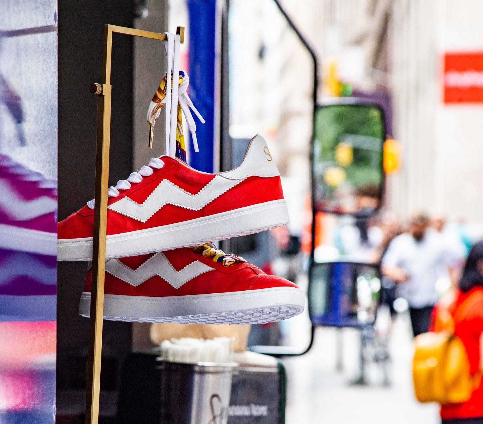 Red and white sneakers with zigzag patterns hang outside against a blurred city street backdrop.
