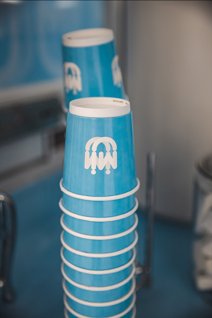 Stack of blue paper cups with a white abstract logo on a countertop in a modern setting.