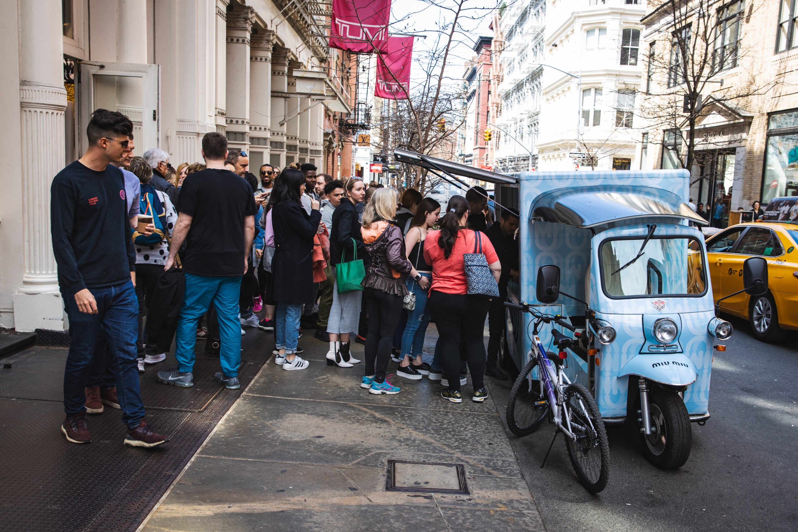 People line up at a blue food truck on a city street, with bikes and buildings nearby.