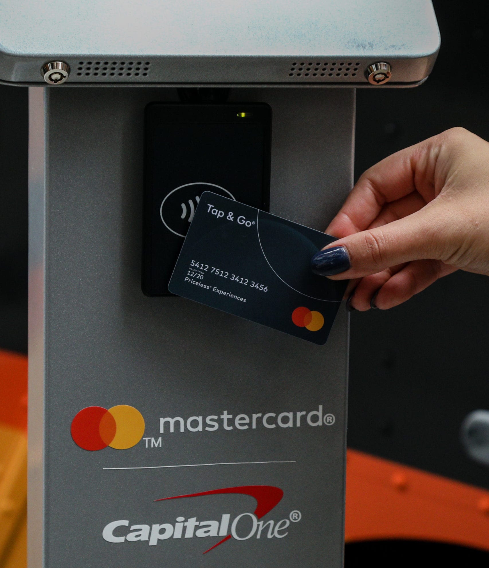 Person holds Mastercard credit card near contactless terminal with Capital One and Mastercard logos.