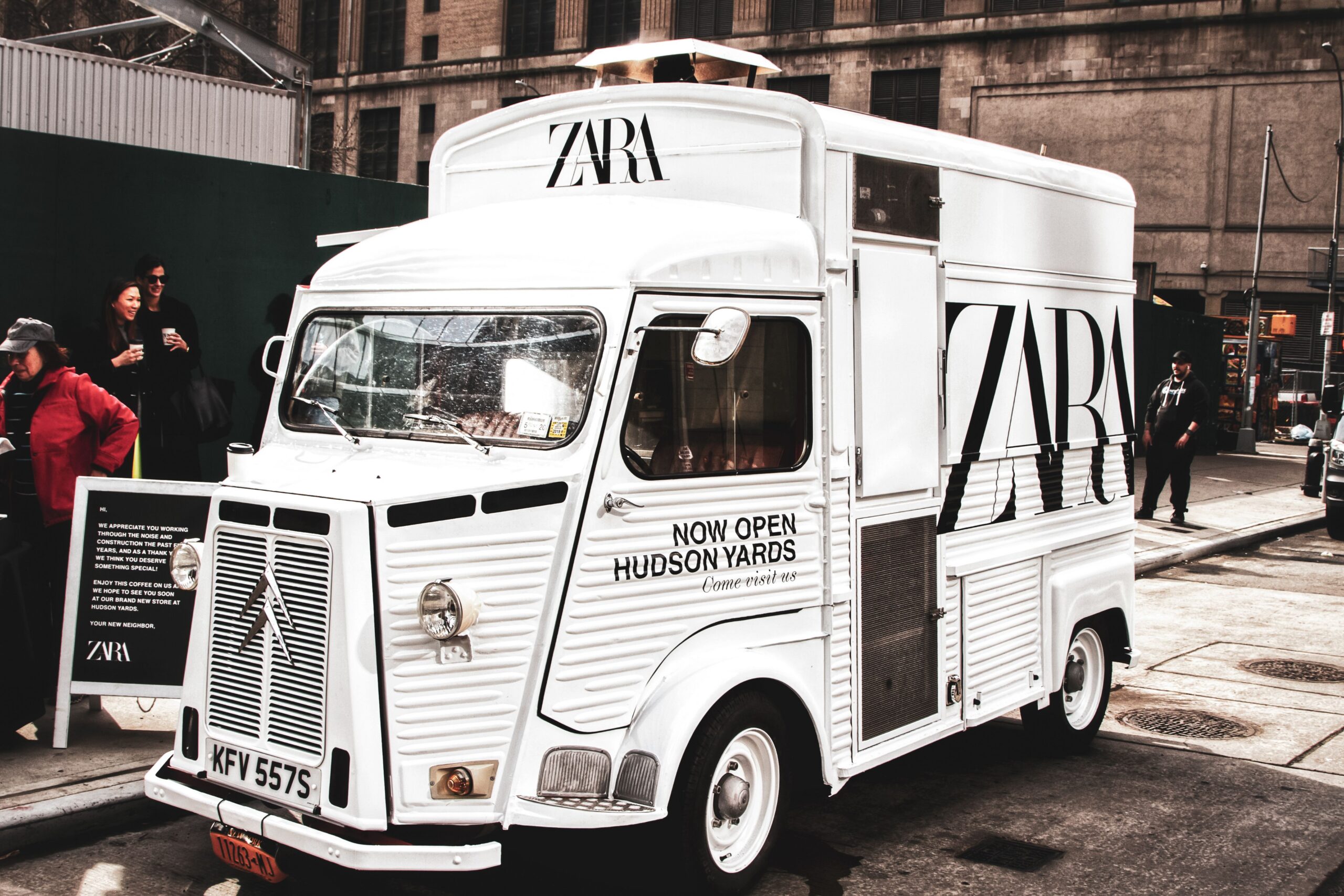White ZARA van with "NOW OPEN HUDSON YARDS" parked on city street near people and tall buildings.