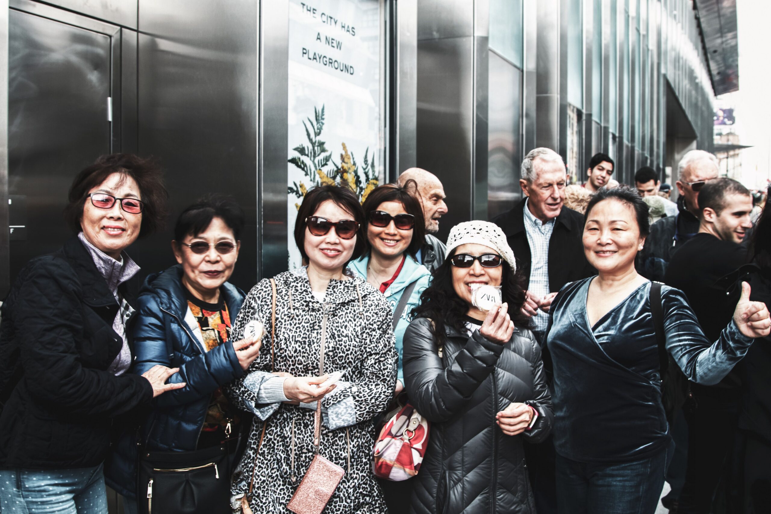 A group poses outside by a reflective building and Experiential Vehicle, some giving thumbs-up.