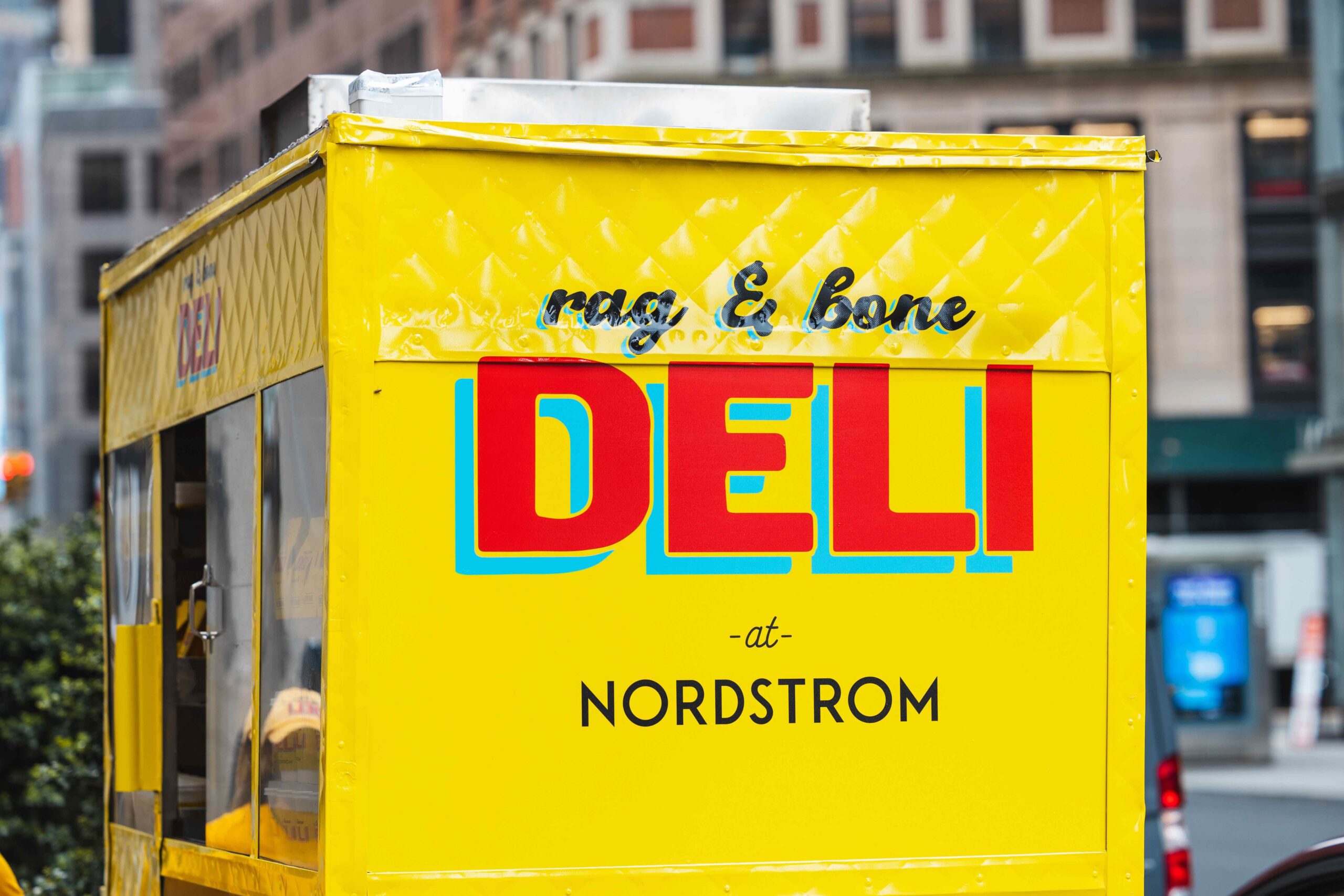 Yellow food cart with “rag & bone DELI at NORDSTROM” lettering on a city street.