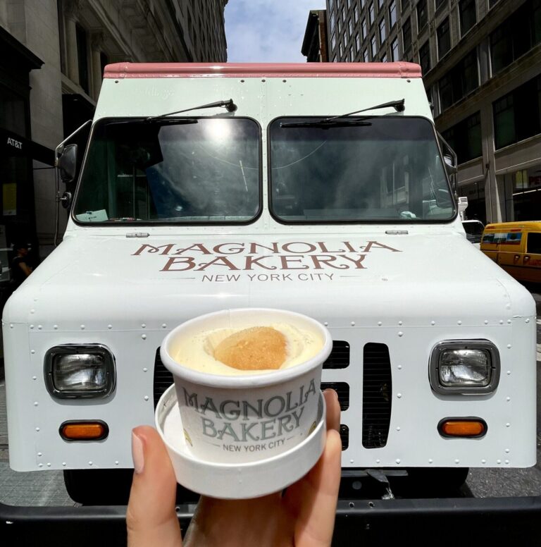 Hand holding Magnolia Bakery dessert in front of bakery truck on a New York City street.