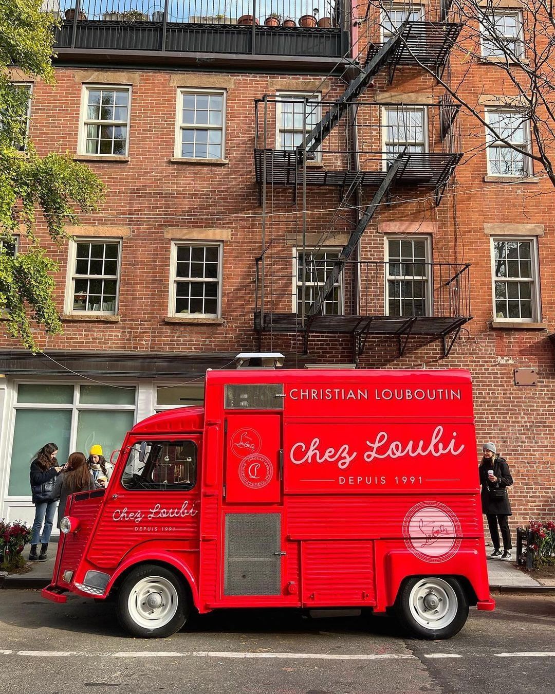 Red "Chez Loubi" food truck parked by a brick building; three people stand on the sidewalk.