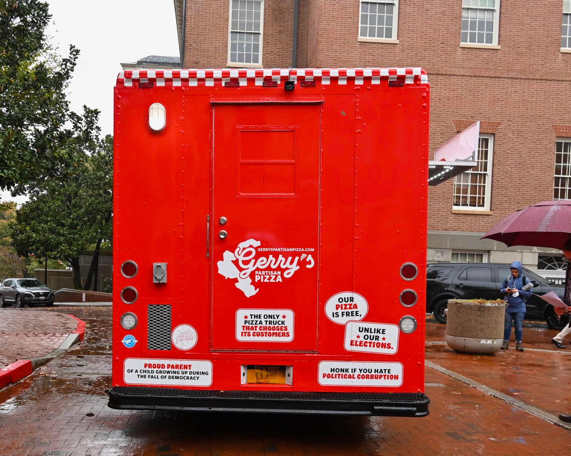 Gerry’s Pizza food truck with slogans is parked on a wet street.