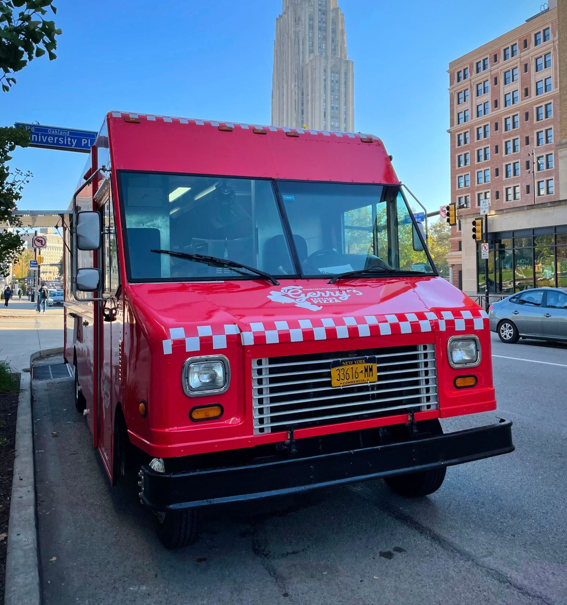 Red Mobile Tour food truck with checkered design parked on a city street near "University Pl" sign.