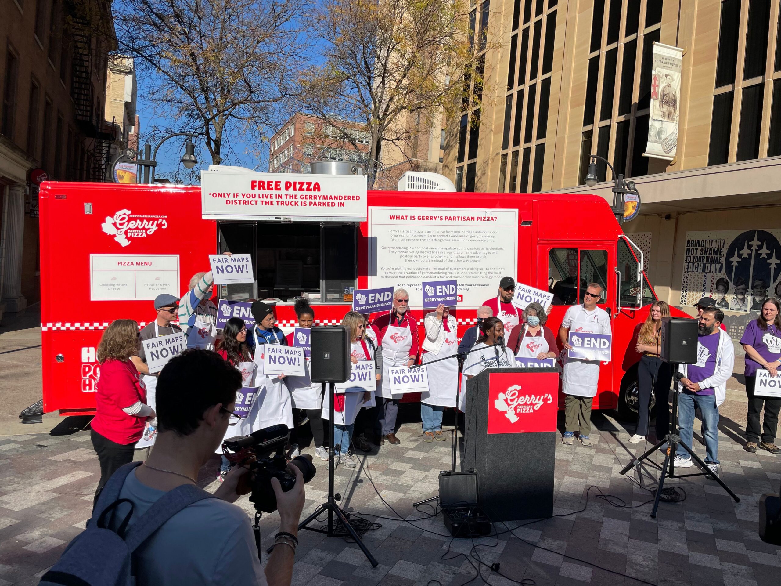 People with Fair Pay NOW and END signs stand by a red Gerry’s Pizza truck at a rally.