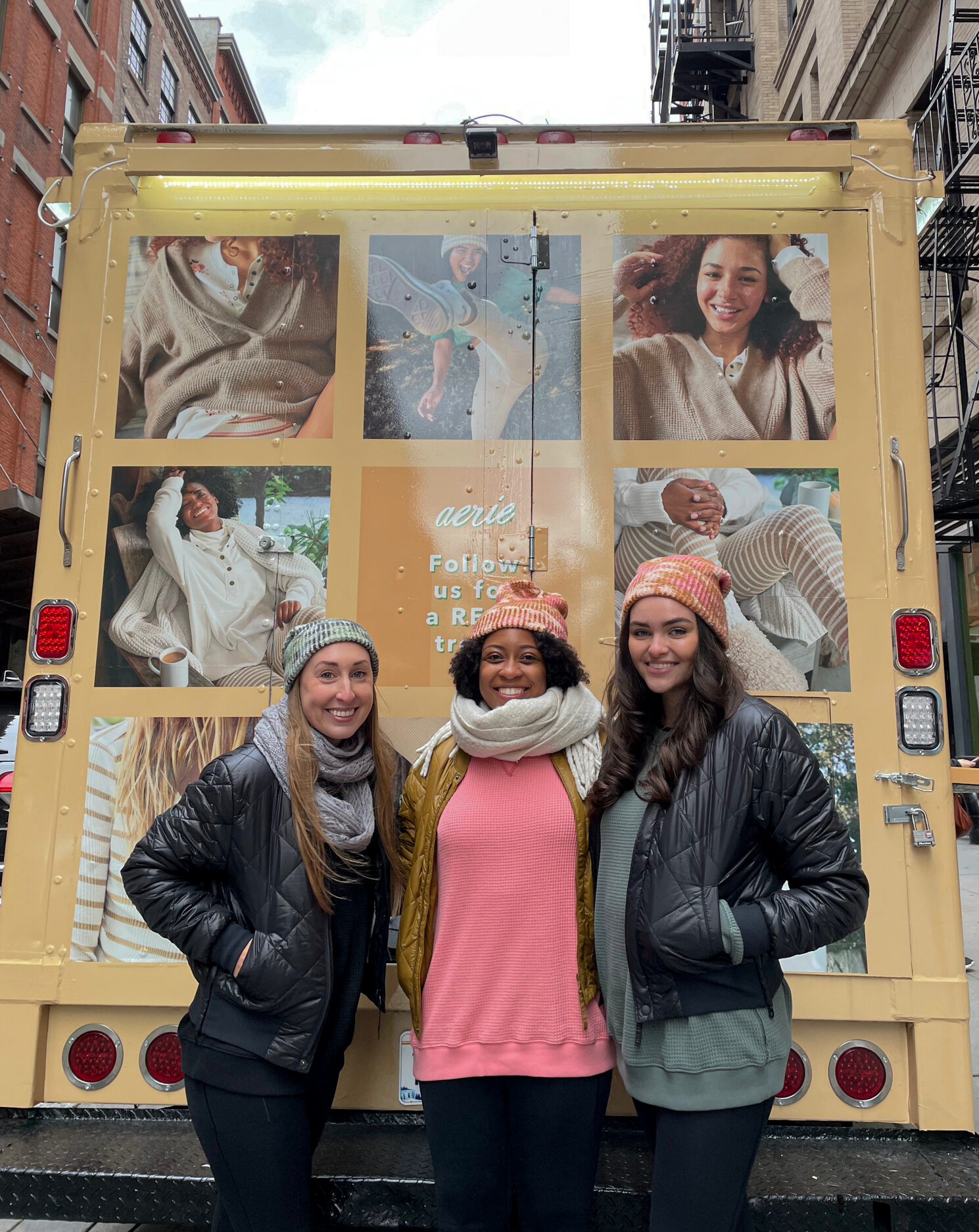 Three women in winter hats and jackets smile in front of an aerie-branded waffle truck.