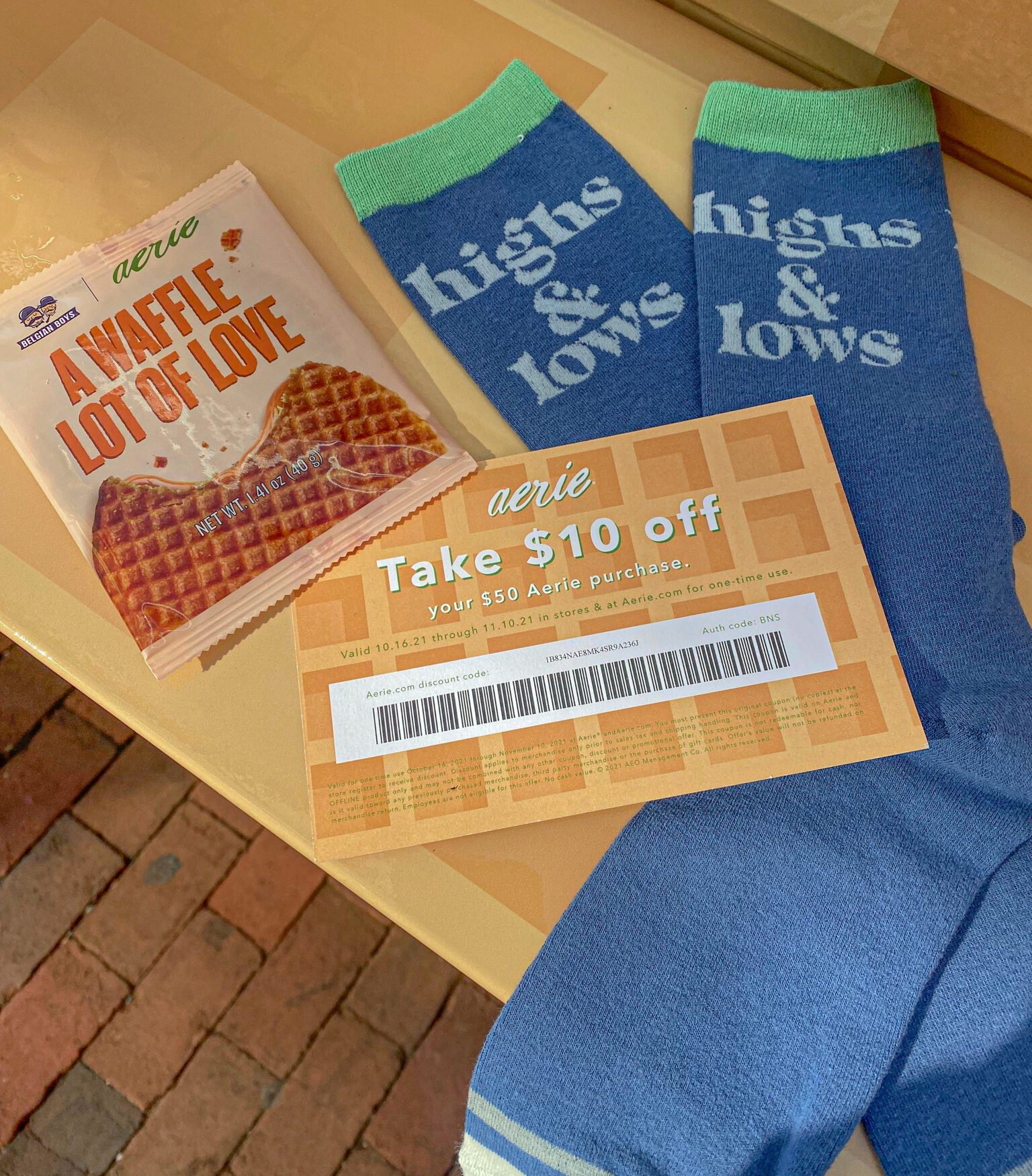 Blue socks with highs & lows text, caramel stroopwafel, and $10 off Aerie coupon on wood surface.