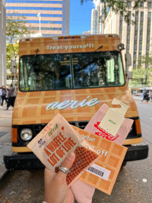 Hand holding a waffle snack, pink socks, and coupon in front of an aerie-branded waffle truck.