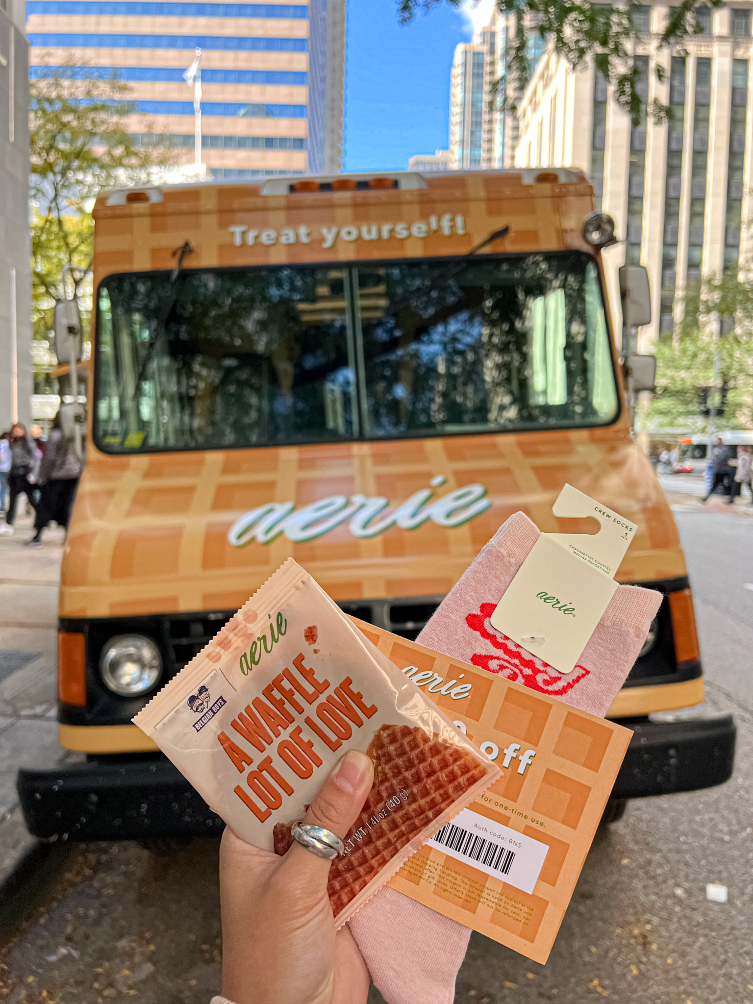 Hand holding a waffle snack, pink socks, and coupon in front of an aerie-branded waffle truck.