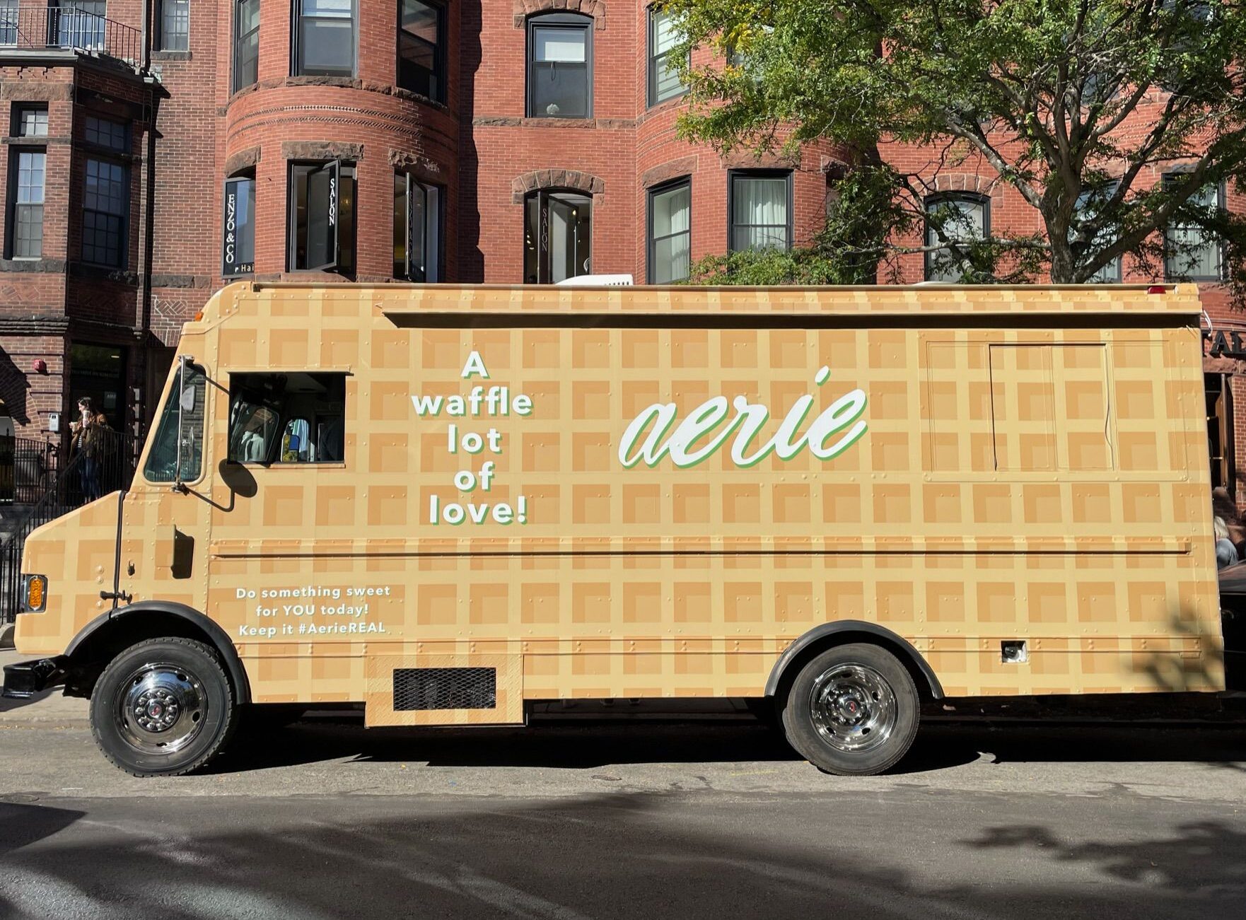 Tan waffle-patterned truck with "A waffle lot of love!" and "aerie" parked on a city street.