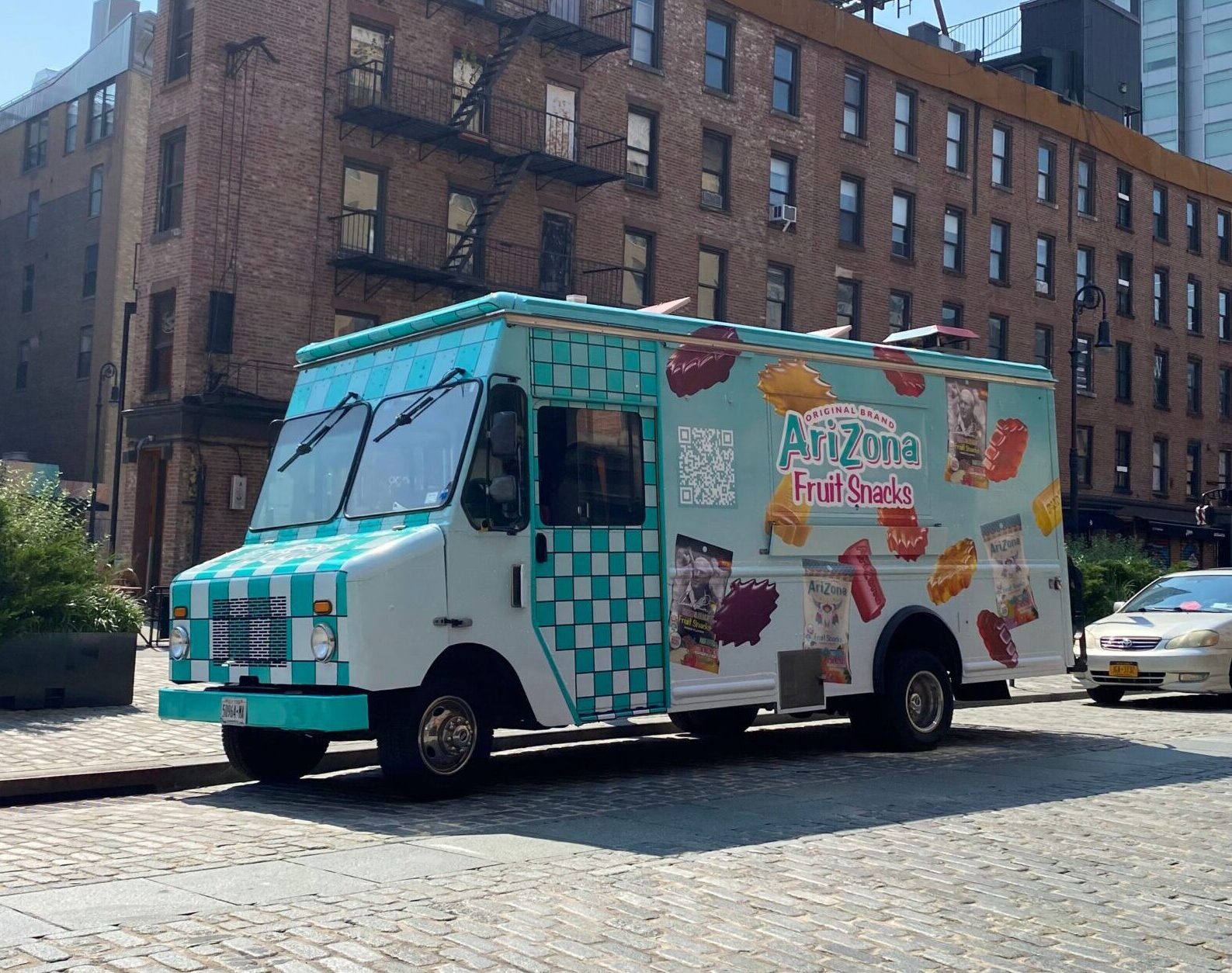 A blue-and-white Arizona Fruit Snacks food truck is parked on a cobblestone city street.
