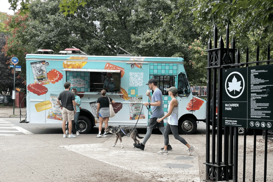 People line up at an ice cream truck near a park entrance, with a dog and McCarren Park sign nearby.