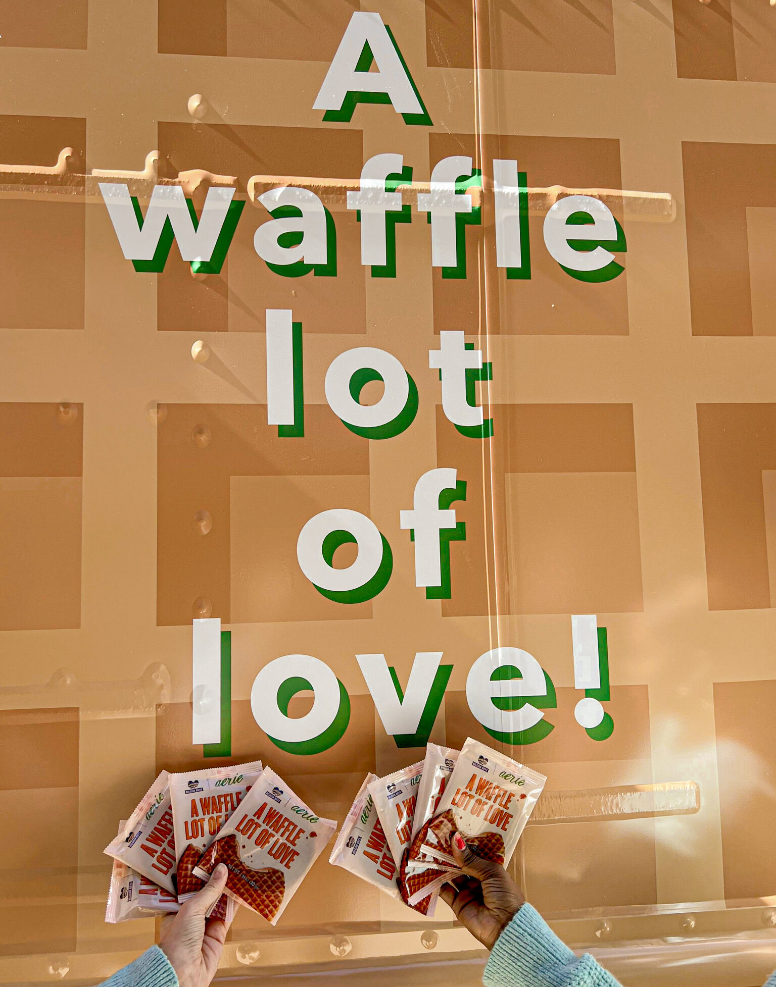 Hands hold waffle snack packs before a waffle-patterned wall with the phrase A waffle lot of love!.