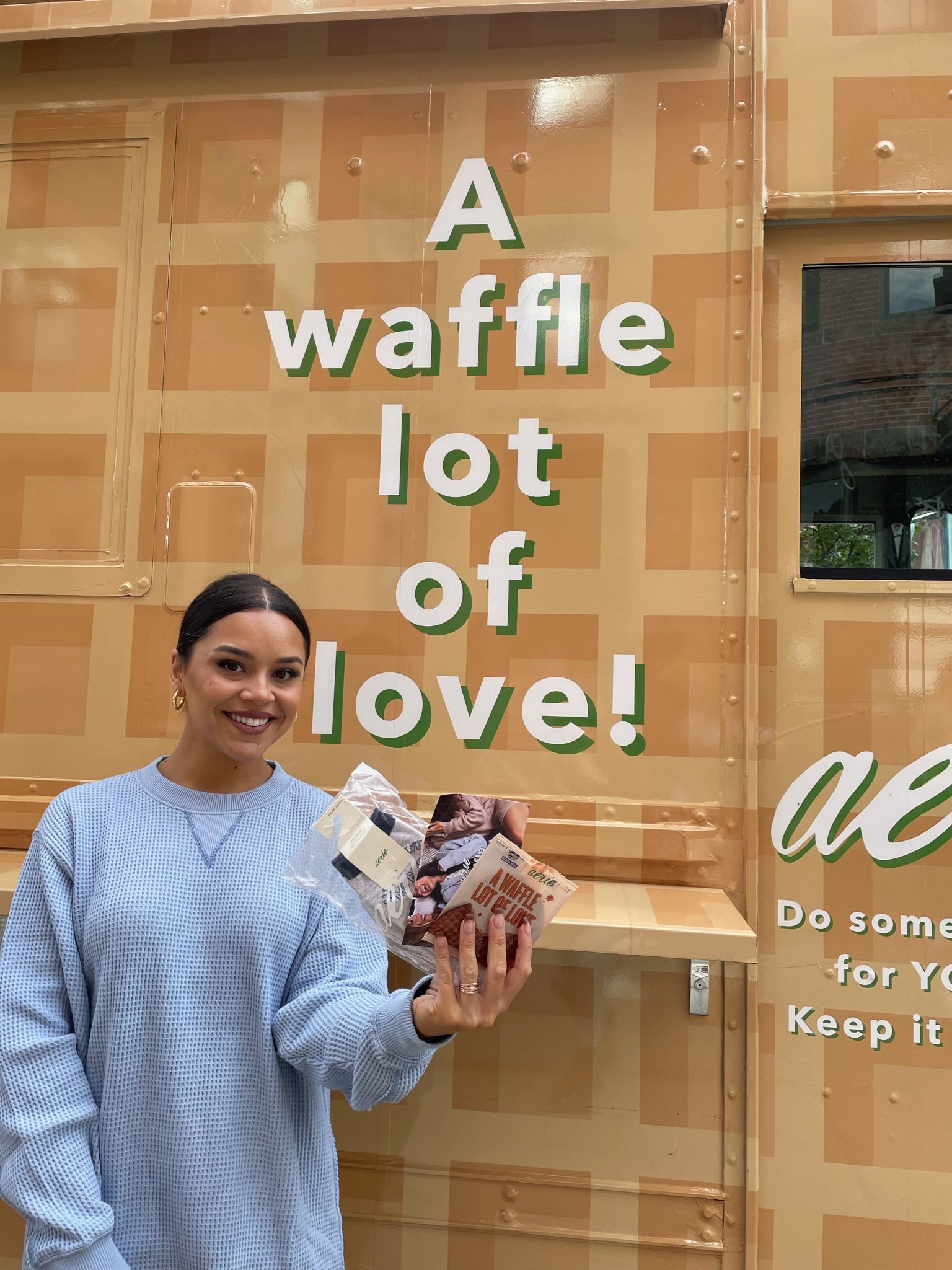 Woman holds a waffle and smiles in front of a waffle truck with “A waffle lot of love!” text.