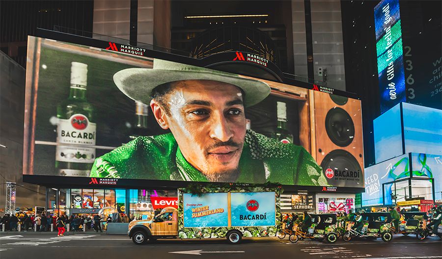Times Square billboard shows man with Bacardi bottles; branded cars and people gather below.