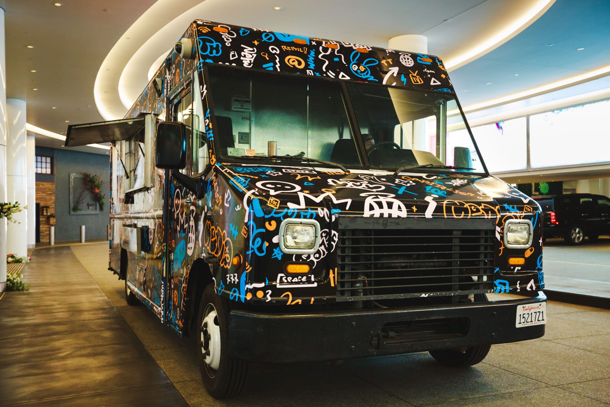 Graffiti-covered food truck with blue, orange, white, and yellow doodles parked indoors.