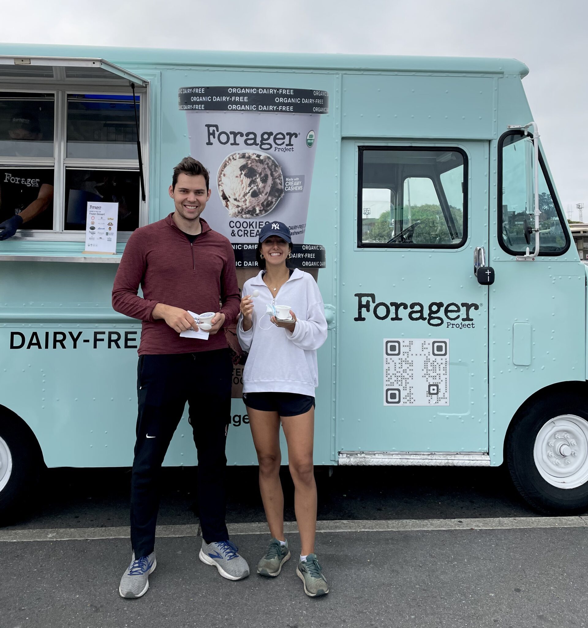 Two people with dairy-free ice cream stand by a Forager food truck with a cookie sign and QR code.