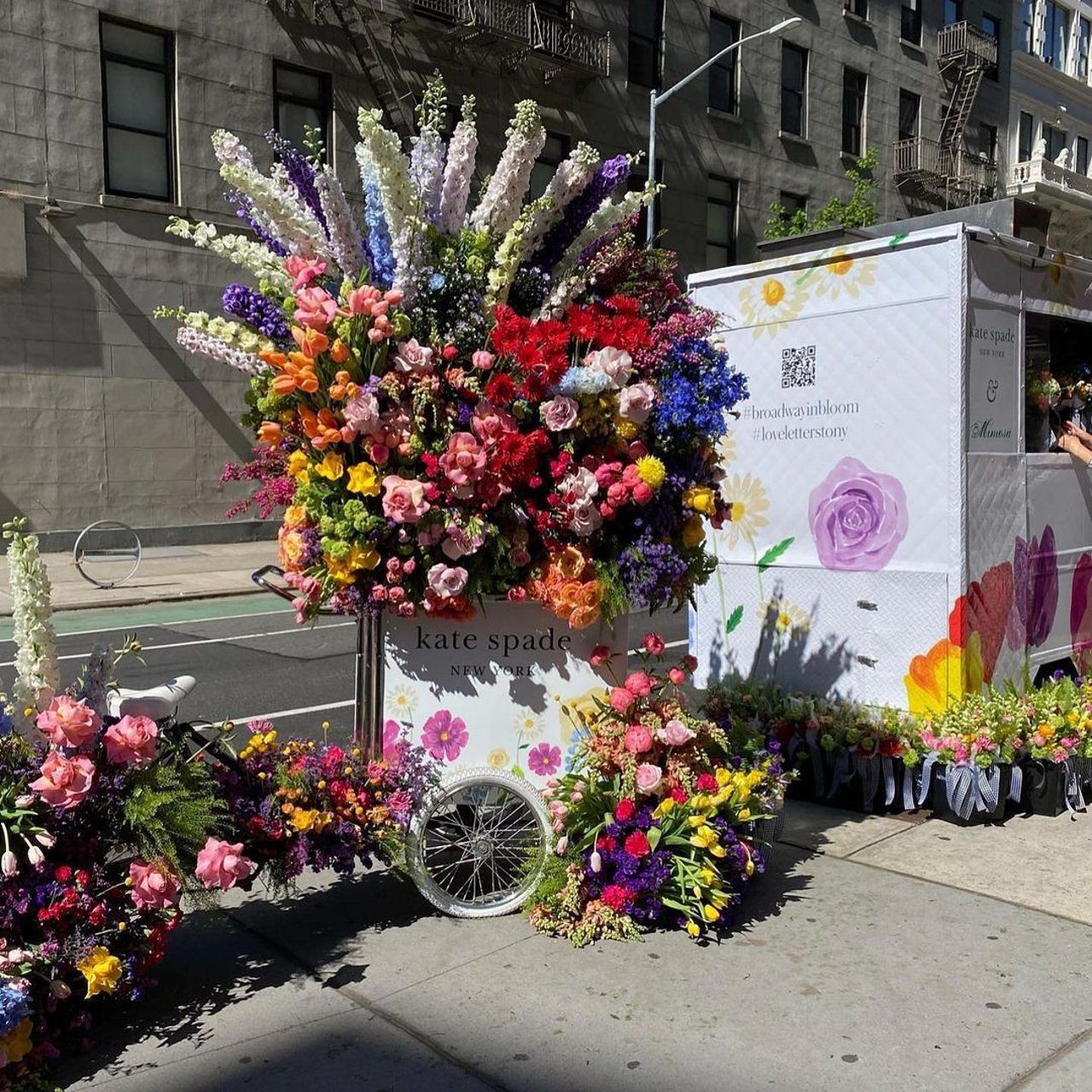 Flower cart with colorful blooms by a white kate spade tent on a city sidewalk.