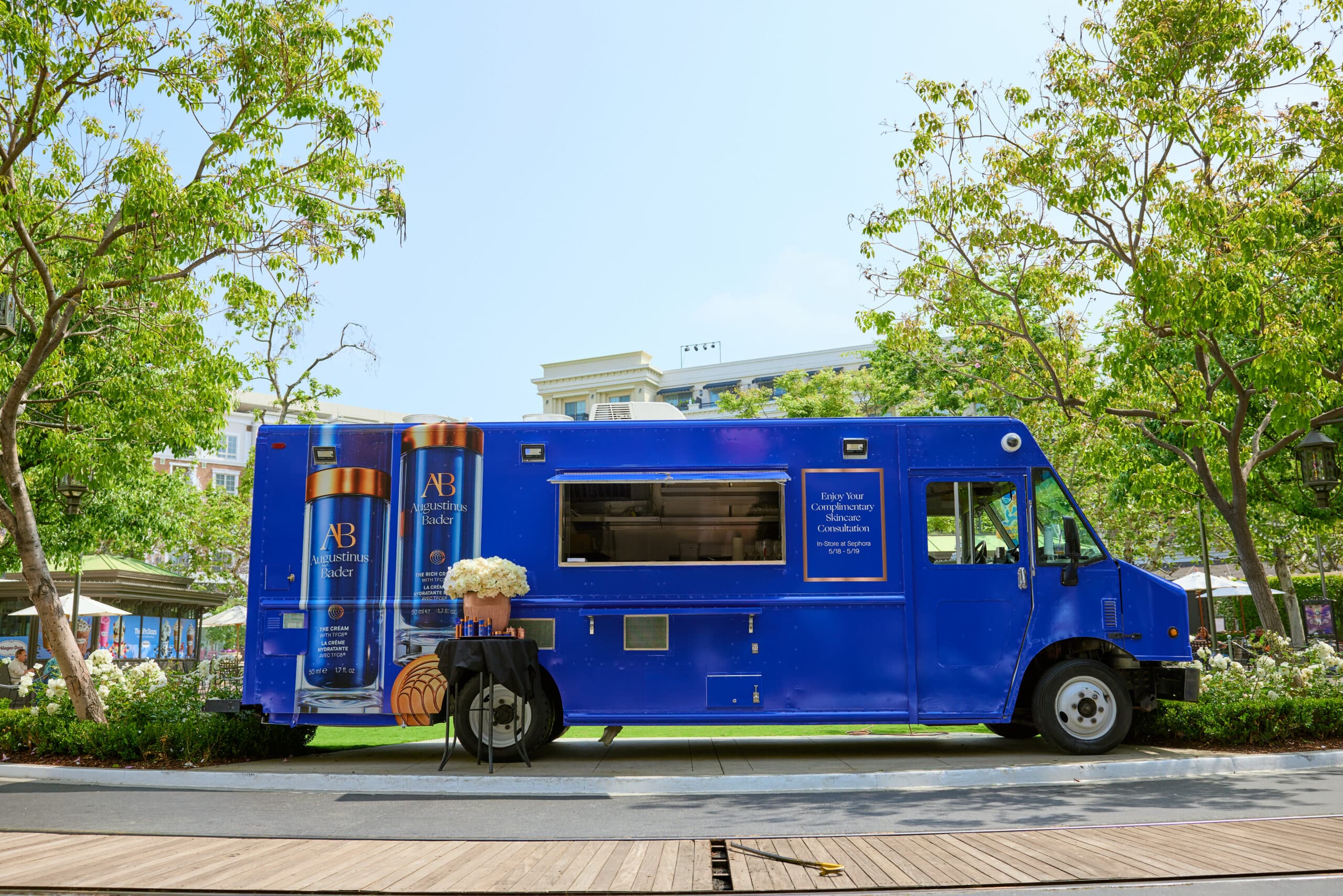 Blue AB-branded food truck parked outdoors beside a table with white flowers and pumpkins.