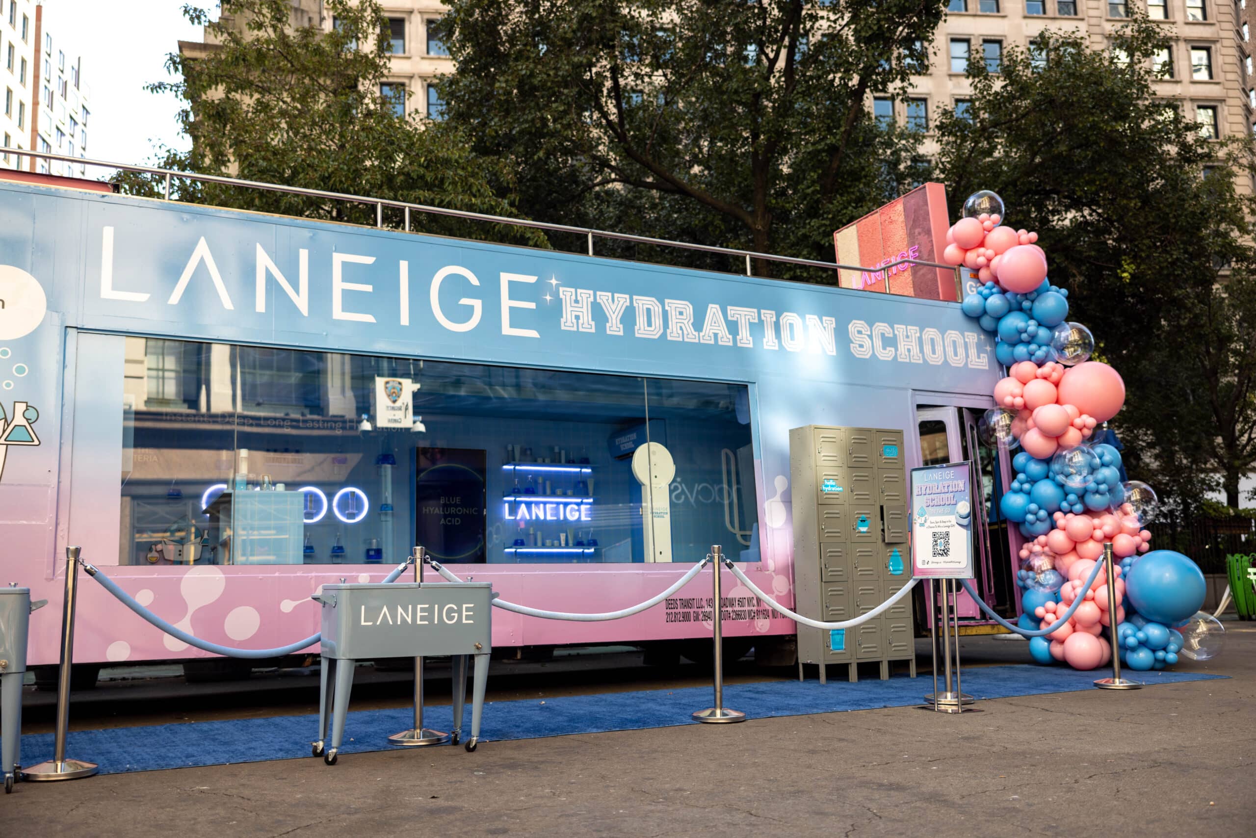 Glass Box Truck labeled Laneige Hydration School with balloons and sign, city buildings behind.