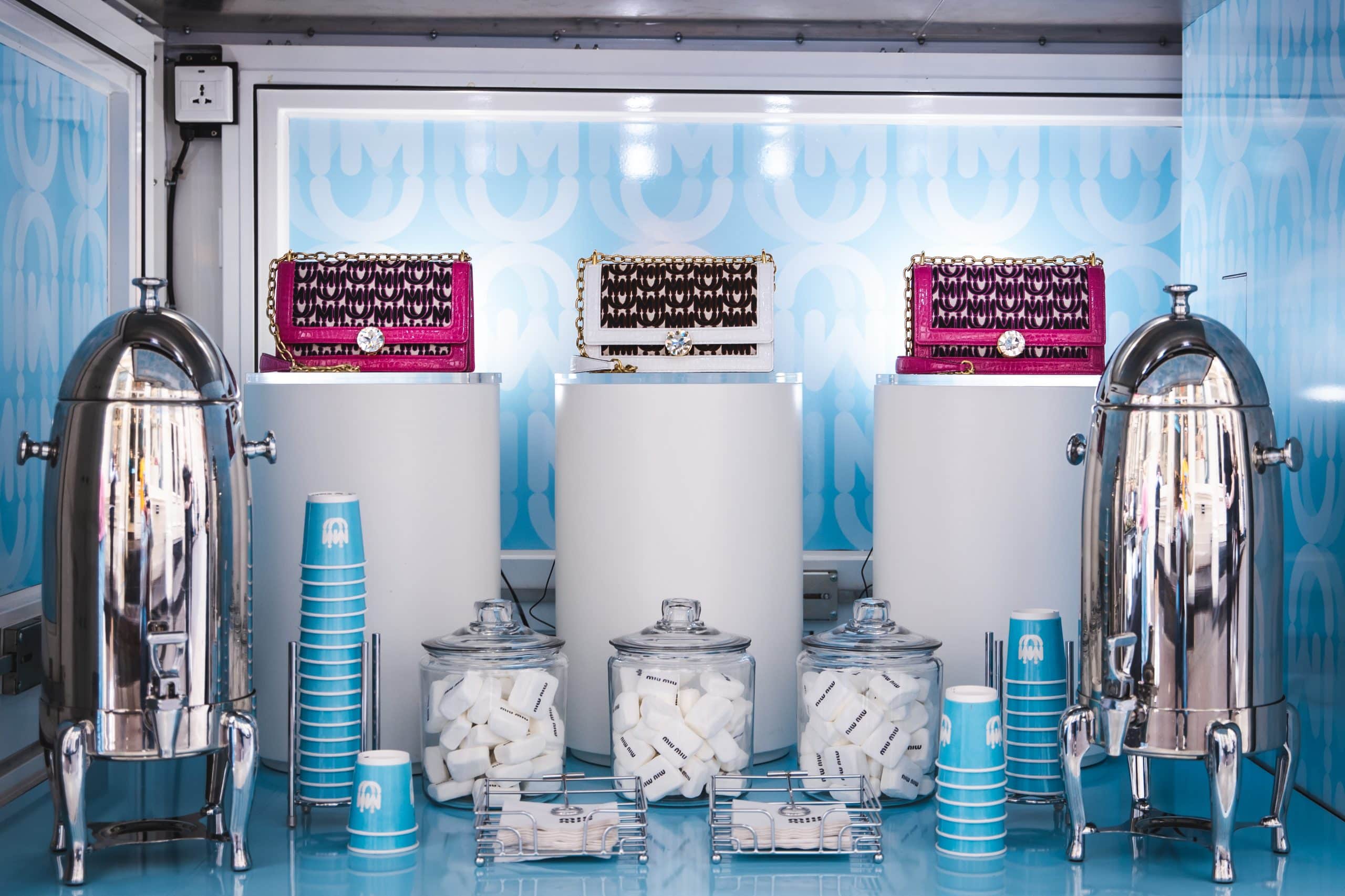 Metal beverage dispensers, blue cups, sugar jars, and decorated boxes on a blue-and-white counter.