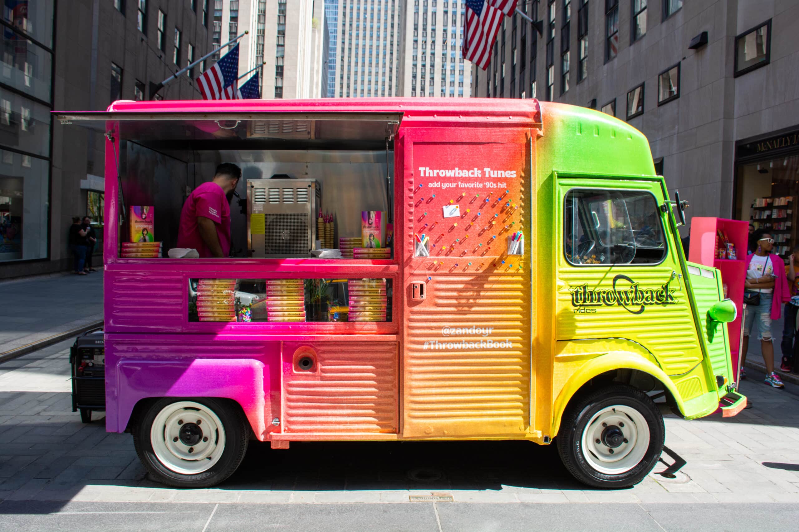 Rainbow Citroens food truck labeled Throwback Tunes serves frozen treats on a city street.