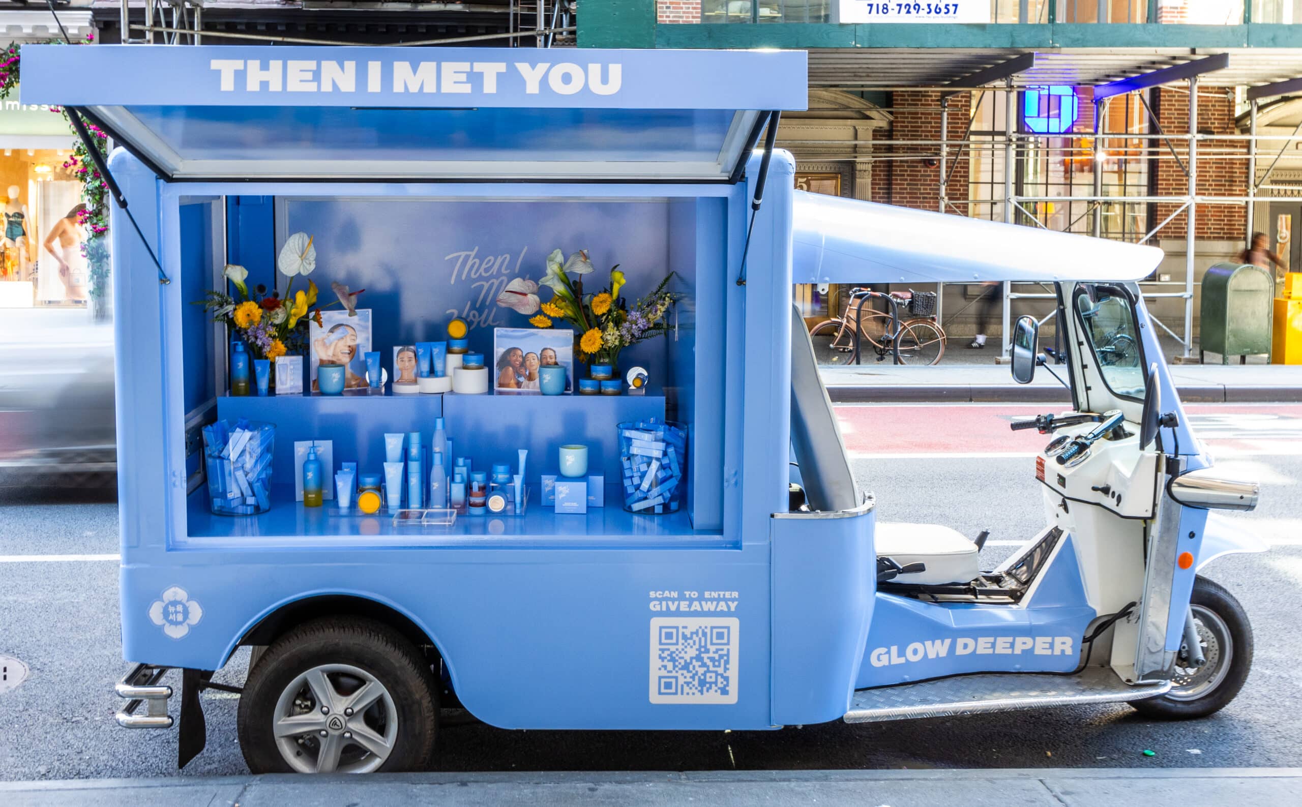 Blue Tuk Tuk with skincare products, flowers, &ldquo;THEN I MET YOU&rdquo; sign, and a giveaway QR code.