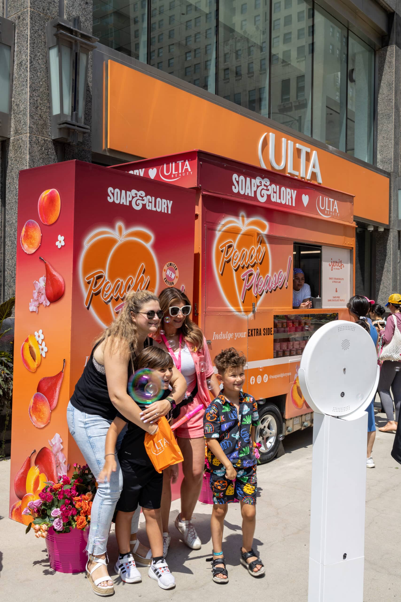 Four people stand before an orange Soap & Glory and Ulta Beauty truck with "Peach Please!" sign.