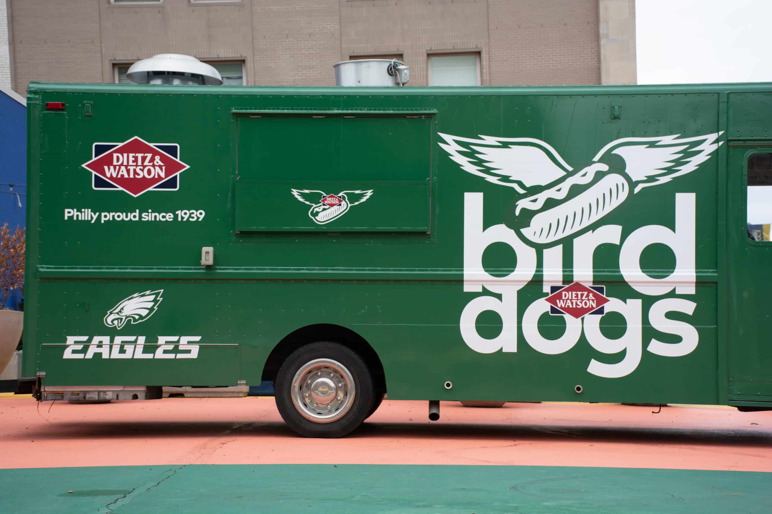 Green food truck with bird dogs, winged hot dog graphic, Eagles and Dietz & Watson logos nearby.