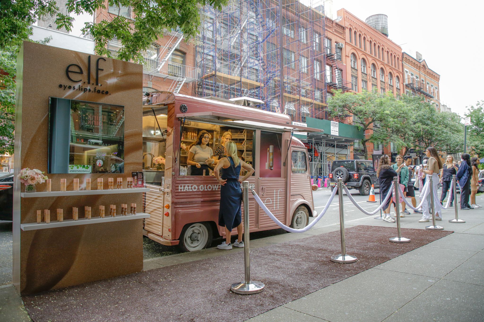 A pink e.l.f. cosmetics truck serves customers on a city street with people lined up outside.