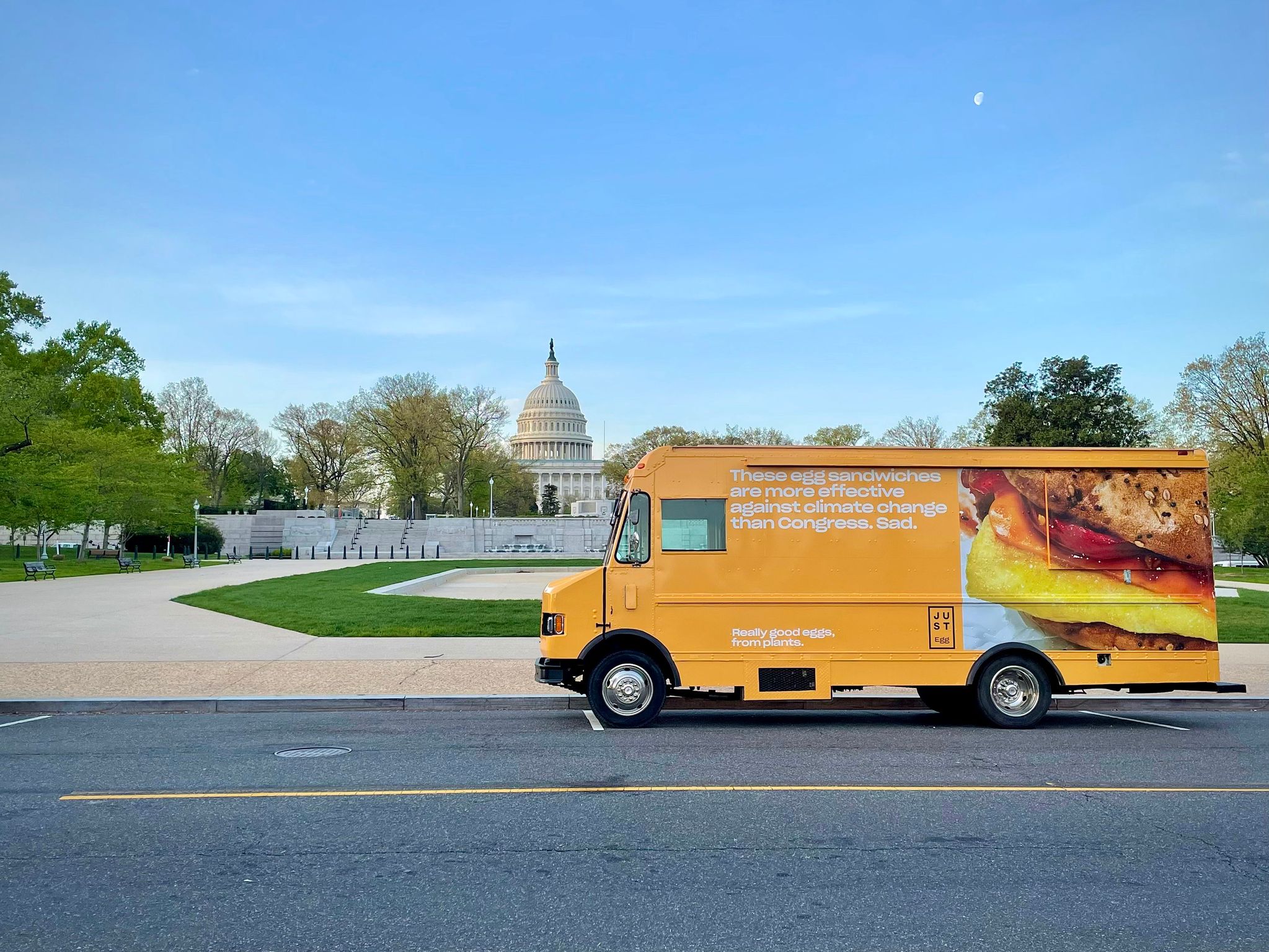 Yellow food truck with sandwich image and climate message parked near the U.S. Capitol.