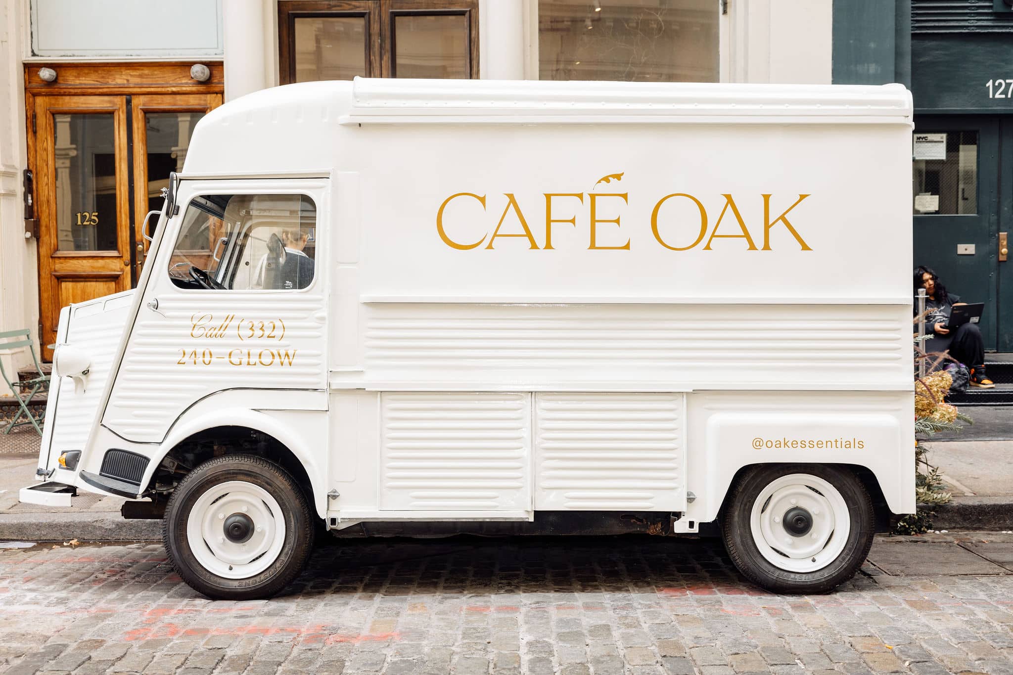 A white vintage Citroens food truck labeled CAF&Eacute; OAK is parked on a cobblestone street.