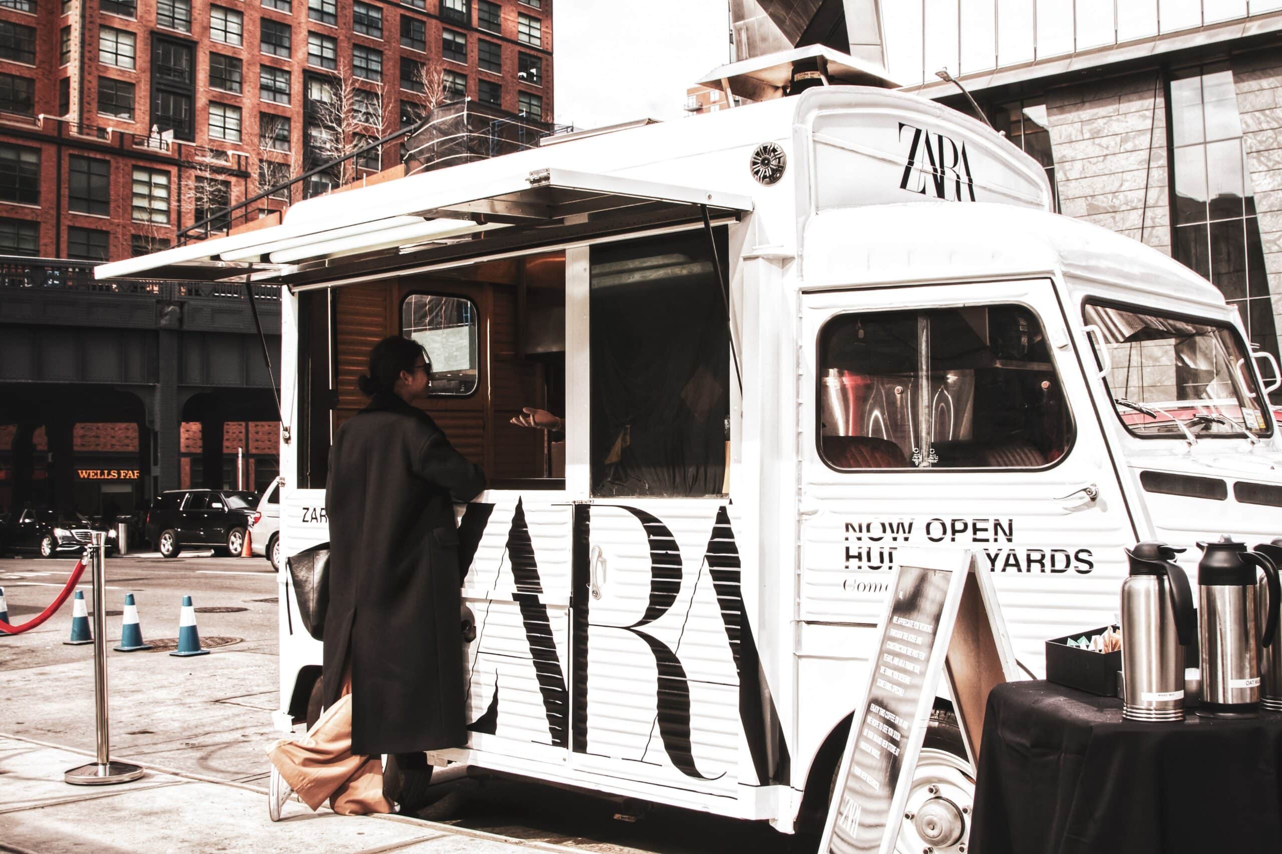 Person at a white Citroens food truck with ZARA branding, parked on a city street.