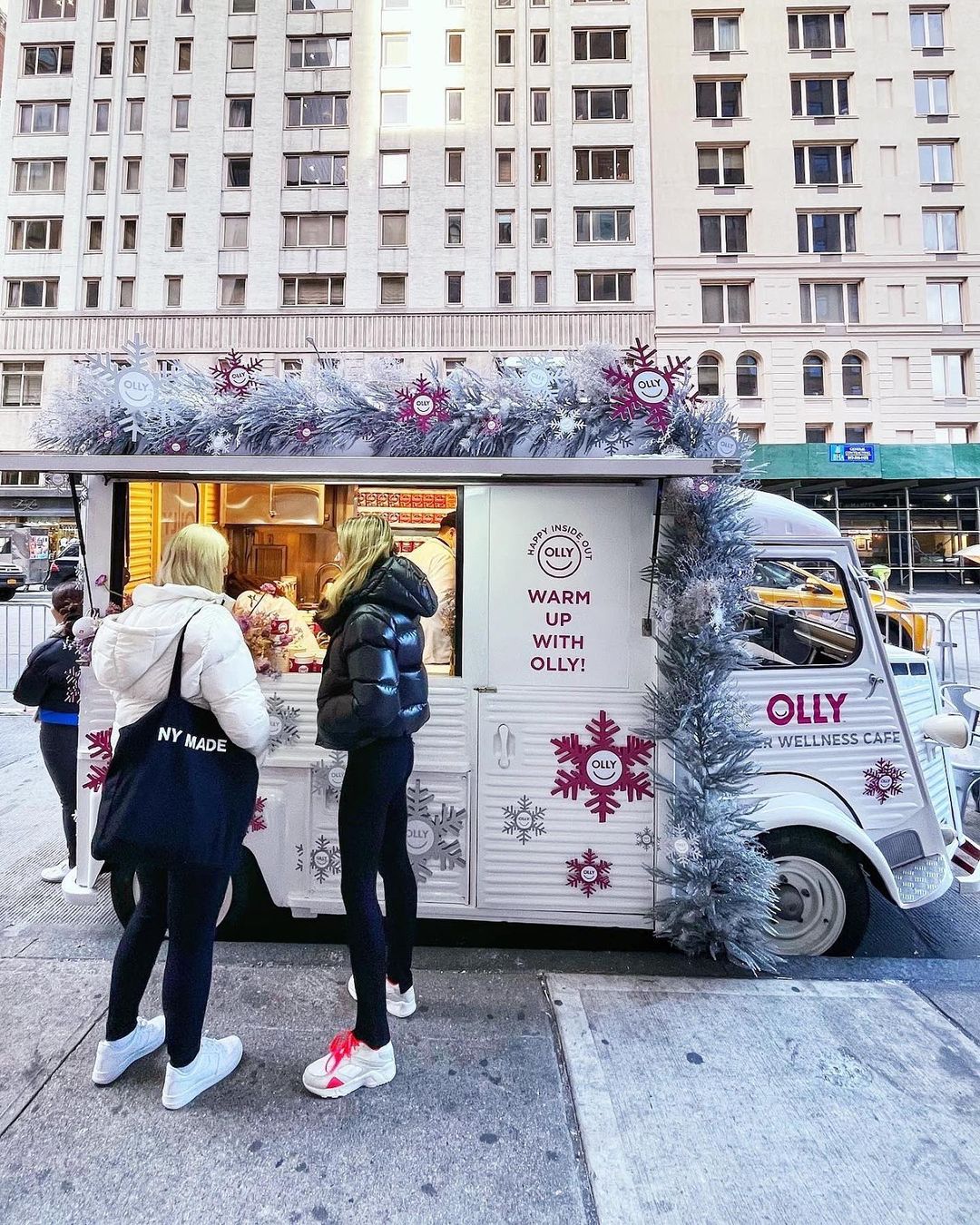 Two people at a holiday-themed food truck with "WARM UP WITH OLLY!" on a city street.