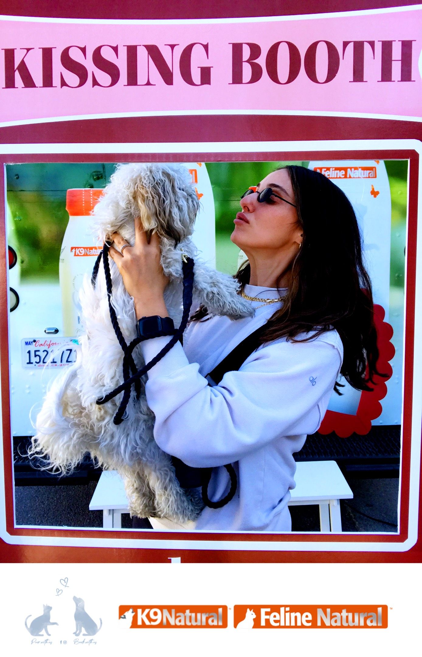 Woman holds up a dog near a KISSING BOOTH sign with K9 Natural and Feline Natural logos.
