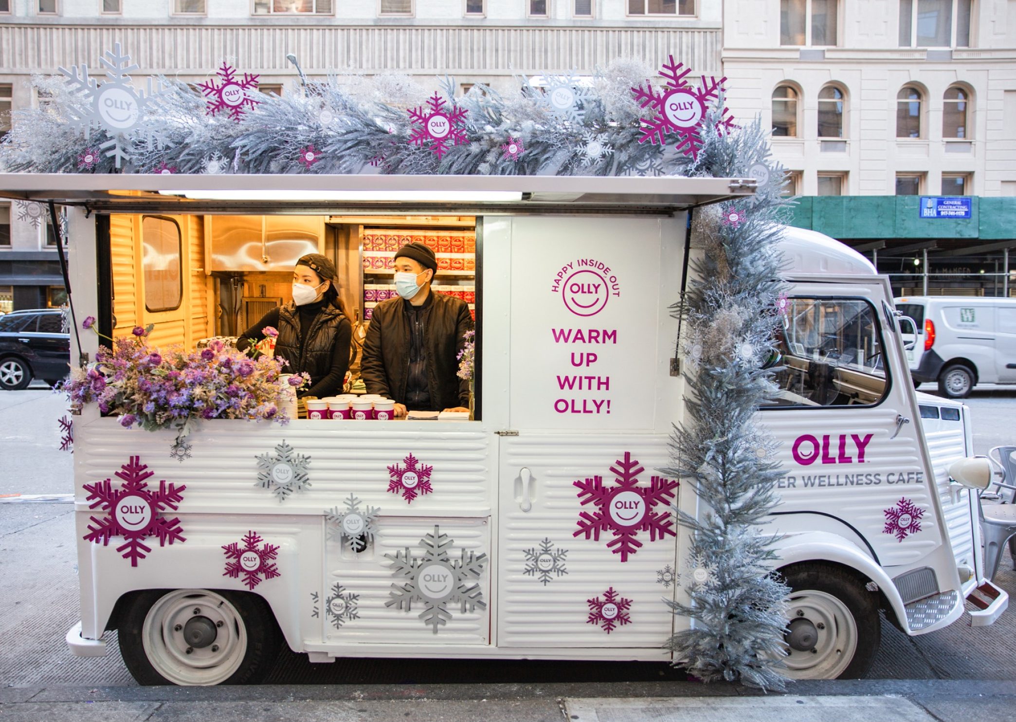 Olly Inner Wellness Café food truck with silver garlands, two masked staff inside serving drinks.