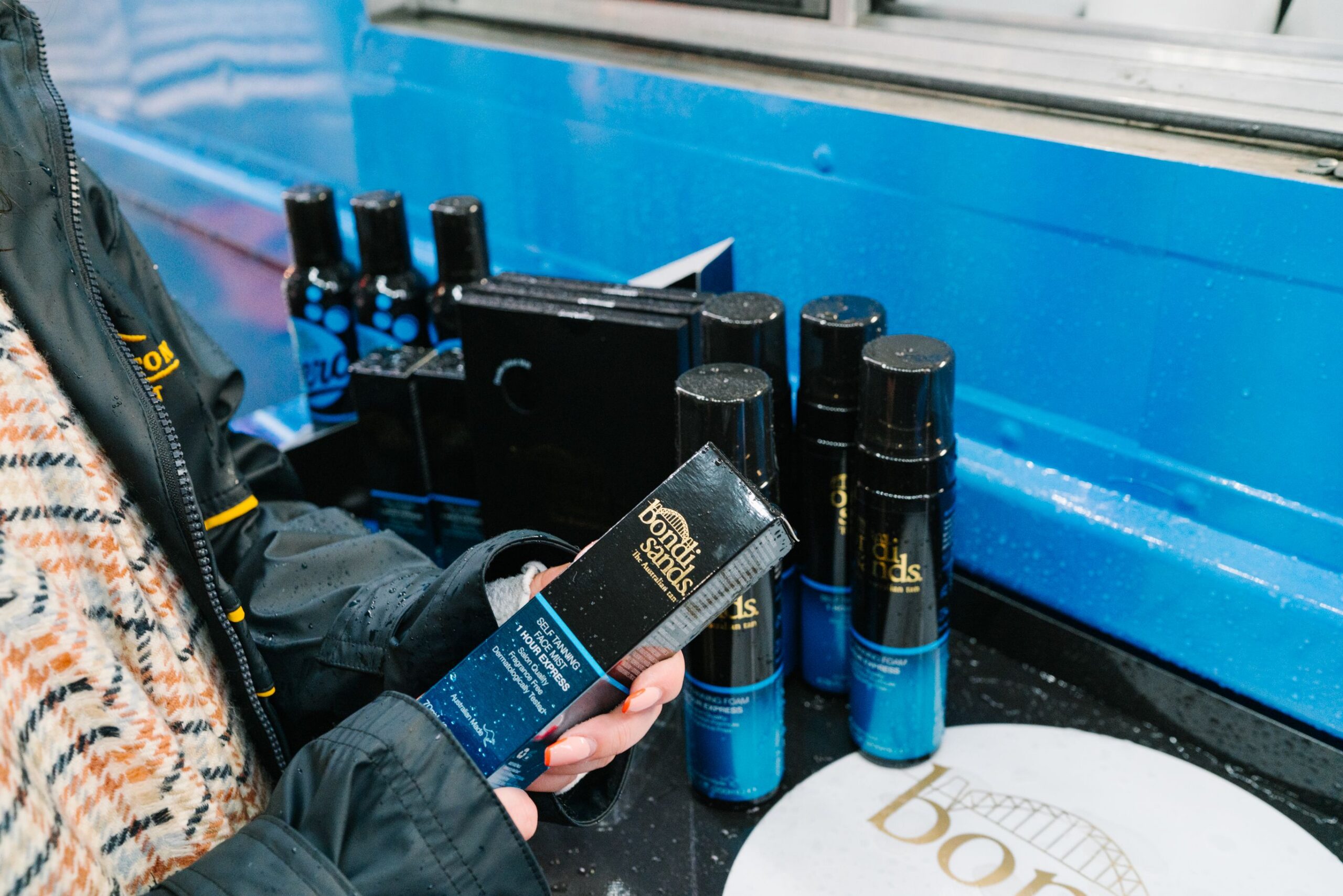 Person holding Bondi Sands Self Tanning Foam box in front of tanning display at beauty pop up.